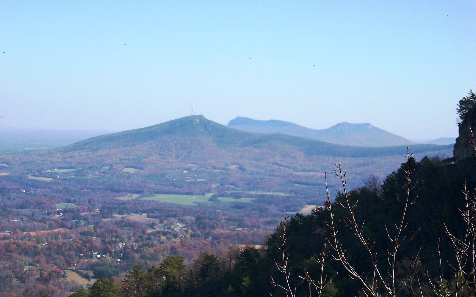 Hazy mountain ridge with a communications tower rises above a patchwork valley of fields and trees